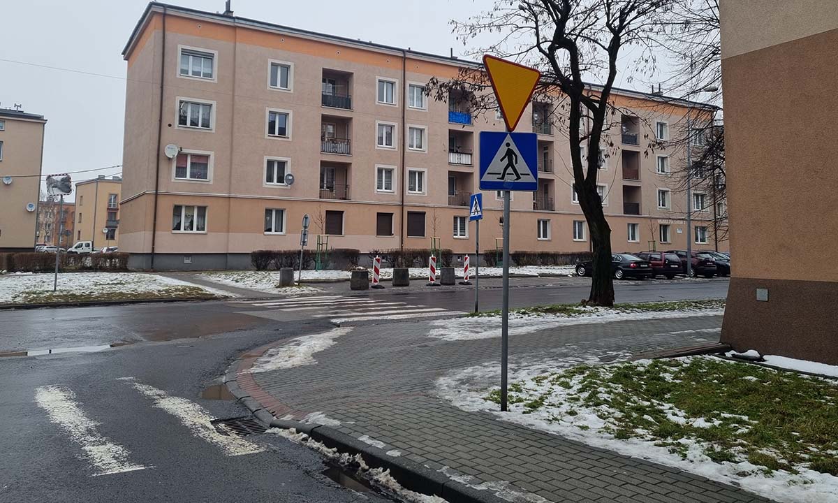 Skrzyżowanie ulic, w prawym rogu w bezpośrednim sąsiedztwie przejścia betonowe bloczki wyłaczają z użycia 3 stanowiska parkingowe