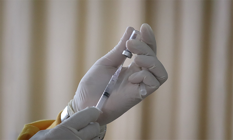 Ręka w białej rękawiczce naciągająca szczepionkę do strzykawki 