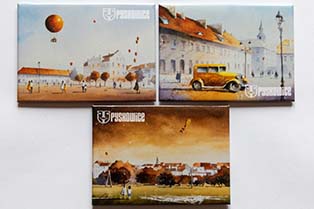 zdjęcie 3 magnesów z grafikami autorstwa Grzegorza Chudego; dwa przedsawiają rynek pyskowicki w róznych ujeciach (na jednym z nich balony, na drugim zabytkowe auto), trzeci magnes to dzieci puszczające latawiec nad rzeką Dramą z panoramą Pyskowic w tle
