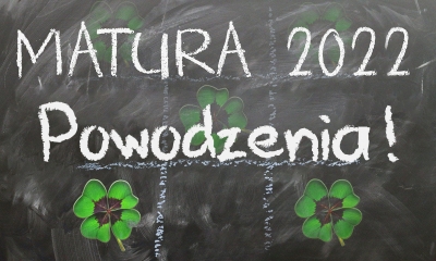 Tablica szkolna, na niej napis Matura 2022 Powodzenia!  i zielone czterolistne koniczynki 