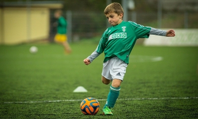 Chłopiec w zielonym stroju składa się do strzału w piłkę nożną, boisko, zielona murawa
