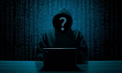 Haker - anonimowa postac, bez twarzy i w kaputrze, siedzi przodem do laptopa na stole. 