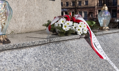 Wiązanka kwiatów z zapalonym zniczem pod pomnikiem 