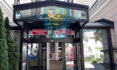 Wejście z przeszkloną witryną do budynku starostwa powiatowego w Gliwicach. W szybach odbija się godło powiatu gliwickiego