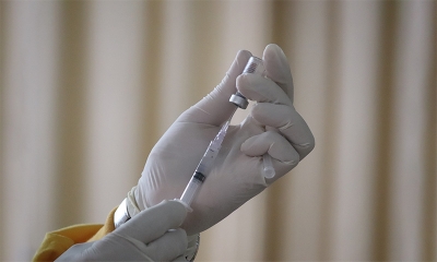 Ręka w białej rękawiczce naciągająca szczepionkę do strzykawki 