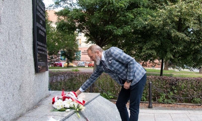 Siwy mężczyzna w garniturze składa wiązankę biało - czerwoną pod monumentem z kamienia