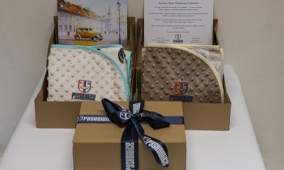 Pakiety powitalne - kocyki z wyszywanym logiem Pyskowic i kartką powitalną, zapakowane w kartonowe pudełko przewiązane wstążką z nadrukiem znaku miasta